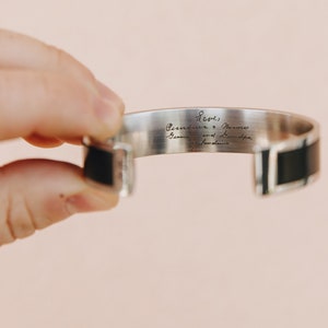 May include: Silver cuff bracelet with a black leather band. The inside of the bracelet is engraved with the text "Love, Grandmother & Nana, Grandma and Linda,  With Love".