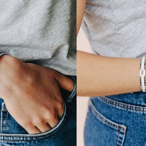 May include: Two silver bracelets with a black and white design. The bracelet on the left has a black band with a silver border. The bracelet on the right has a white band with a silver border and an infinity symbol.