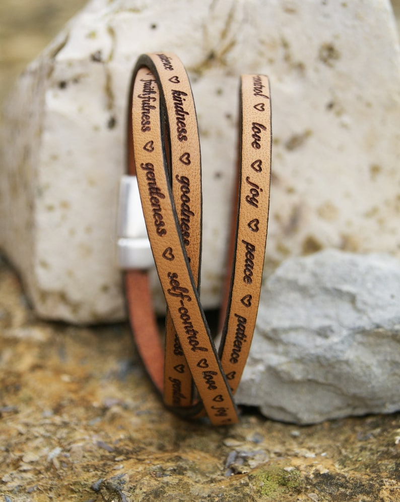 Puede incluir: Un brazalete de cuero de triple vuelta con las palabras "paciencia", "paz", "alegr&iacute;a", "amor", "autocontrol", "bondad", "amabilidad", "fidelidad", "mansedumbre" grabadas en &eacute;l.
