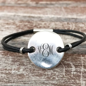 Può includere: Un braccialetto in pelle nera con un ciondolo rotondo in argento inciso con il monogramma "WEM".