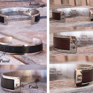 May include: A silver cuff bracelet with black leather detailing. The inside is engraved with "Forever Always". The front of the bracelet features engraved coordinates. The ends of the bracelet have the letter "K" engraved.
