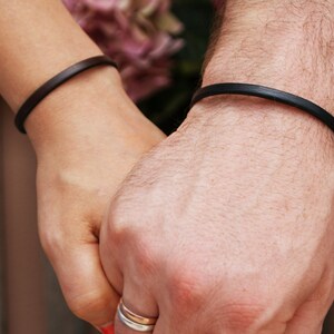 May include: Two people holding hands, each wearing a simple black leather bracelet.