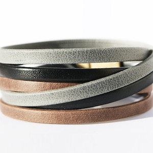 Puede incluir: Un brazalete de múltiples capas hecho de cuero marrón, negro y gris. El brazalete está tejido en un patrón de cruz.