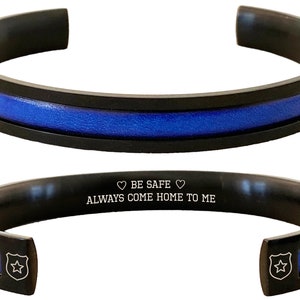 May include: Black stainless steel bracelet with a blue line and an engraved message: "BE SAFE ALWAYS COME HOME TO ME".