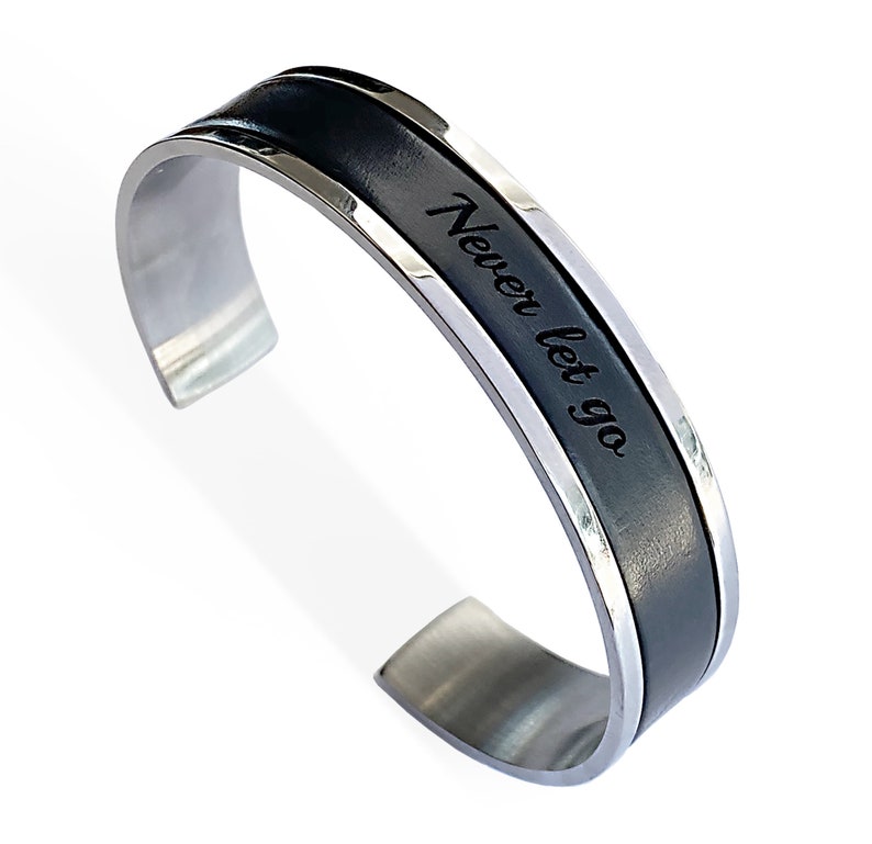 May include: A silver and black stainless steel cuff bracelet with the words "Never let go" engraved on the black band.