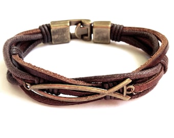 Puede incluir: Un brazalete de cuero marrón con un diseño tejido y un dije de pescado de metal.