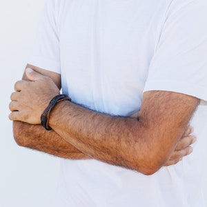 May include: A close-up of a person's arm wearing a brown leather bracelet with black stitching.