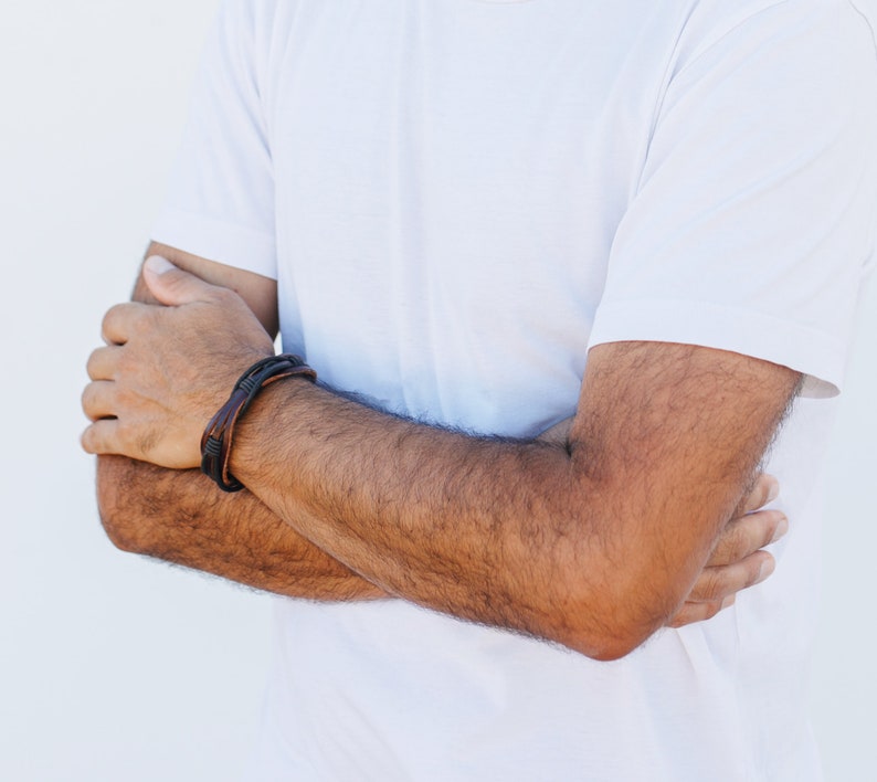 May include: A close-up of a person's arm wearing a brown leather bracelet with black stitching.