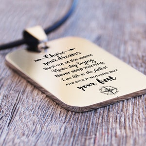May include: Silver necklace with a rectangular pendant engraved with the inspirational quote "Chase your dreams, Burst out at the seams, Never stop trying, Never stop learning, Live life to the fullest, AND GIVE IT NOTHING BUT your best." A compass symbol is at the bottom of the pendant.