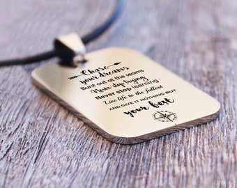 May include: Silver necklace with a rectangular pendant engraved with the inspirational quote "Chase your dreams, Burst out at the seams, Never stop trying, Never stop learning, Live life to the fullest, AND GIVE IT NOTHING BUT your best." A compass symbol is at the bottom of the pendant.