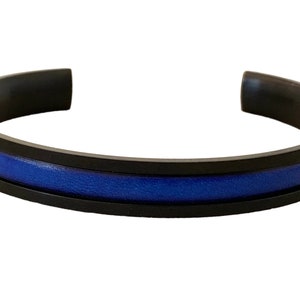 May include: A black metal bracelet with a blue leather inlay. The bracelet is a simple design with a thin blue stripe in the centre.
