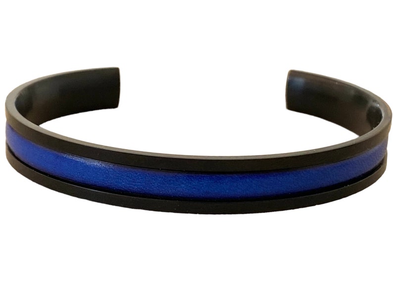 May include: A black metal bracelet with a blue leather inlay. The bracelet is a simple design with a thin blue stripe in the centre.