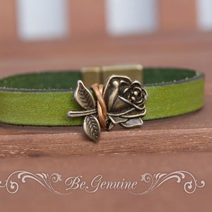 May include: A green leather bracelet with a metal rose charm. The rose is a vintage style and has a copper wire wrapped around it.