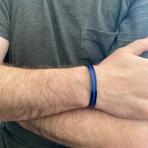 May include: A black bracelet with a thin blue stripe. The bracelet is worn on a person's wrist.
