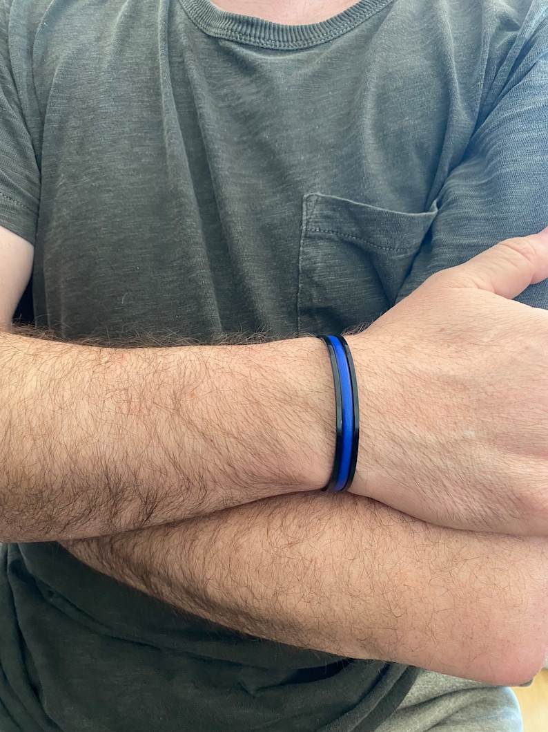 May include: A black bracelet with a thin blue stripe. The bracelet is worn on a person's wrist.