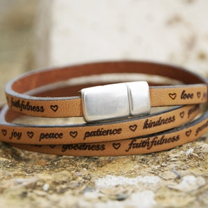 Puede incluir: Un brazalete de cuero marr&oacute;n con cierre de plata. El brazalete tiene las palabras "love", "joy", "peace", "patience", "kindness", "goodness" y "faithfulness" grabadas.