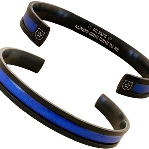 May include: Black stainless steel bracelet with a blue line and a police badge engraved on it. The bracelet has the inscription "Always come home to me. Be safe."