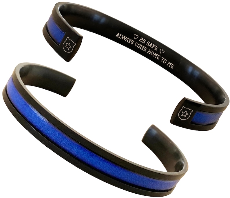 May include: Black stainless steel bracelet with a blue line and a police badge engraved on it. The bracelet has the inscription "Always come home to me. Be safe."