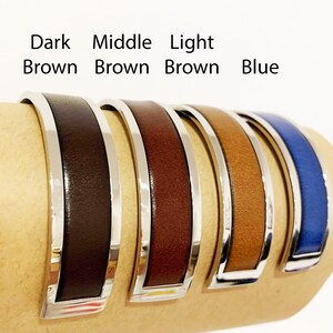 May include: Five leather cuff bracelets in shades of brown and blue, each with a silver-tone metal frame. The bracelets are displayed side by side, with the text "Dark Brown, Middle Brown, Light Brown, Blue" above them.