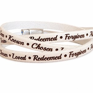 Puede incluir: Una pulsera envolvente blanca con texto grabado en marr&oacute;n oscuro que incluye las palabras Seen, Known, Redeemed, Forgiven, Adopted, Chosen y Loved, separadas por peque&ntilde;os puntos. La pulsera tiene un cierre magn&eacute;tico de metal plateado.