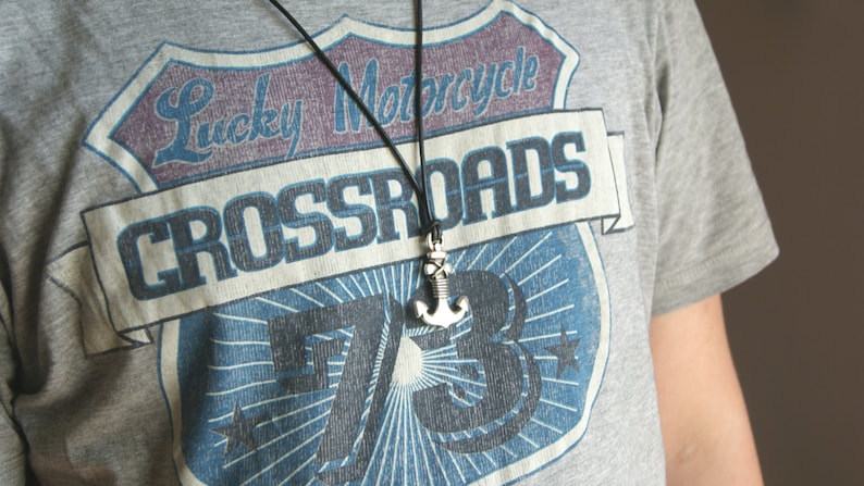May include: A gray t-shirt with a vintage-style graphic of a motorcycle club patch. The patch features the text "Lucky Motorcycle Crossroads 73" and a stylized anchor.
