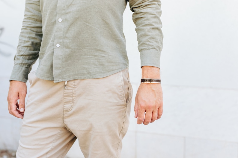 May include: A man wearing a light green button-down shirt and beige pants. He is wearing a brown leather bracelet with a silver buckle on his right wrist.