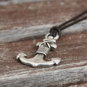 May include: A silver anchor pendant on a brown leather cord necklace.