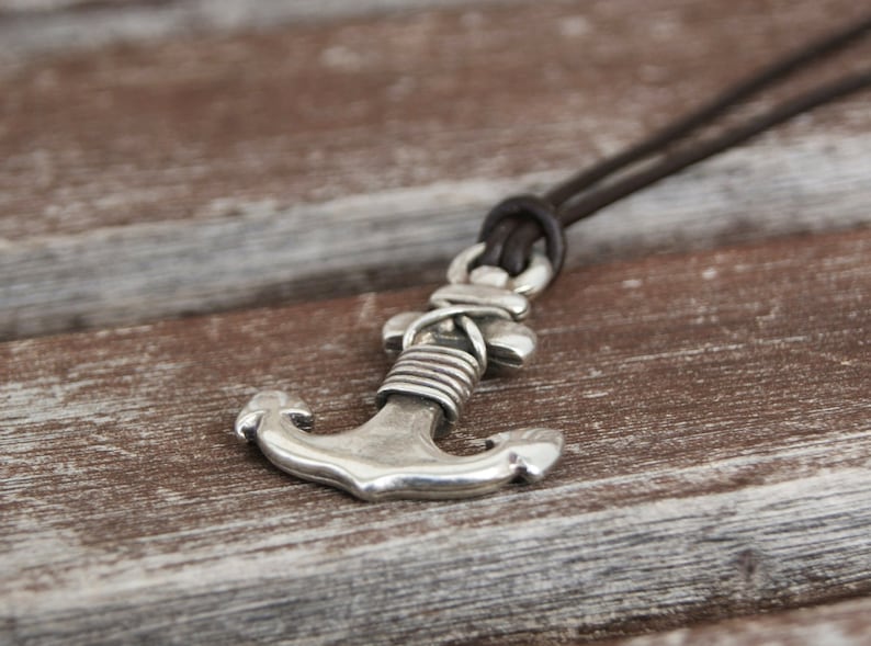 May include: A silver anchor pendant on a brown leather cord necklace.
