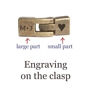 May include: A gold-toned metal clasp with an engraved heart on the smaller part and the initials "M+J" on the larger part.