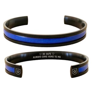 May include: Black stainless steel bracelet with a blue leather inlay and an inscription that reads "Be Safe, Always Come Home To Me".