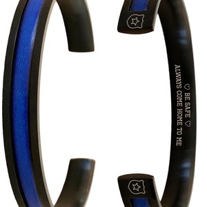 May include: Black and blue stainless steel bracelet with a thin blue line and a star-shaped badge charm. The bracelet has the inscription "BE SAFE ALWAYS COME HOME TO ME".