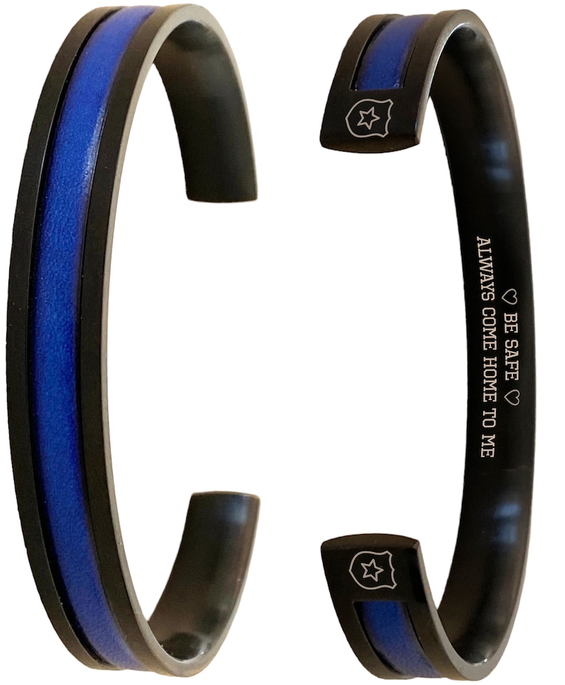 May include: Black and blue stainless steel bracelet with a thin blue line and a star-shaped badge charm. The bracelet has the inscription "BE SAFE ALWAYS COME HOME TO ME".