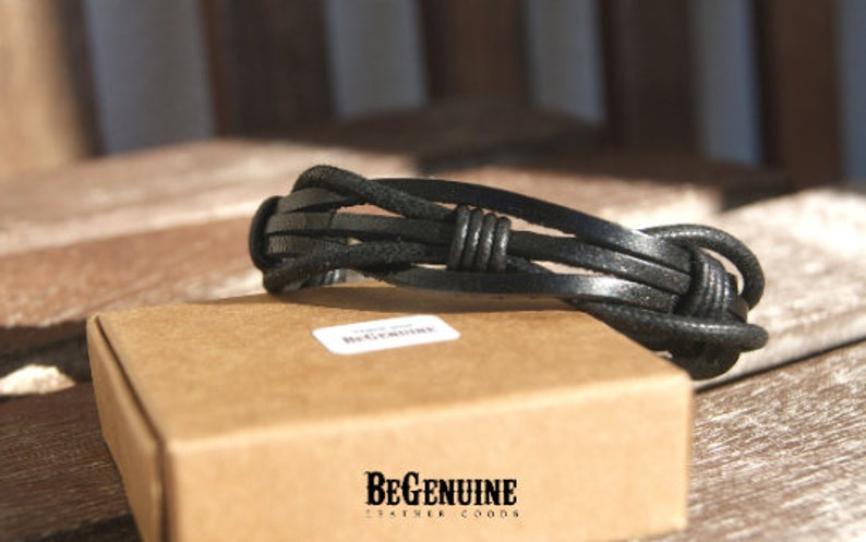 May include: Black leather bracelet with a braided design and a knot detail. The bracelet is on a brown box with the text "BeGenuine Leather Goods".