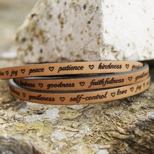 Puede incluir: Un brazalete de cuero marr&oacute;n con las palabras "love, joy, peace, patience, kindness, goodness, faithfulness, gentleness, self-control, love, joy" grabadas en &eacute;l.