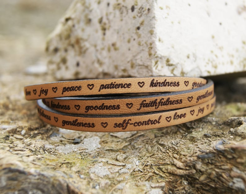 Puede incluir: Un brazalete de cuero marr&oacute;n con las palabras "love, joy, peace, patience, kindness, goodness, faithfulness, gentleness, self-control, love, joy" grabadas en &eacute;l.