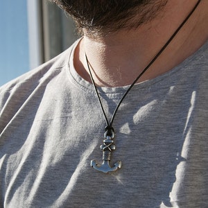 May include: A silver anchor pendant necklace on a black leather cord. The anchor has a rope design and is a popular nautical theme.