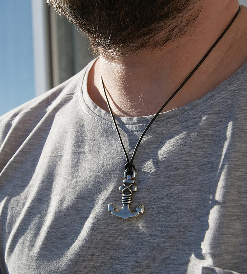May include: A silver anchor pendant necklace on a black leather cord. The anchor has a rope design and is a popular nautical theme.