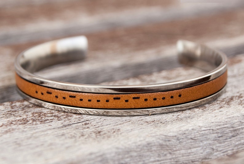 A leather cuff bracelet with a stainless steel band with Morse code engraved. Stainless steel adjustable bracelet with custom morse code engraved makes meaningful long distance relationship gift for boyfriend or girlfriend.
