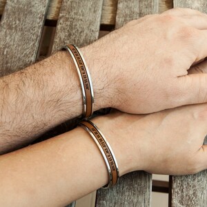 May include: Two leather bracelets with silver metal bands. The bracelets have engraved text that reads "We met in the summer of 9 19 15 5:00 PM".