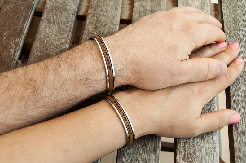 May include: Two leather bracelets with silver metal bands. The bracelets have engraved text that reads "We met in the summer of 9 19 15 5:00 PM".