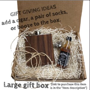 May include: A brown wooden box with a brown and silver flask and a small bottle of Jack Daniel's Tennessee Whiskey inside. The box is filled with shredded paper. The text "GIFT GIVING IDEAS add a cigar, a pair of socks, or booze to the box." is printed on the top of the box. The text "Large gift box (link to purchase this item is in the "item description")" is printed below the box.
