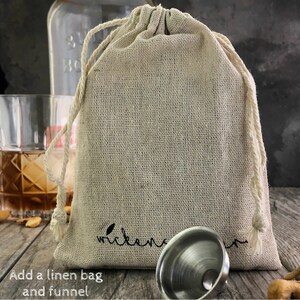 May include: A natural linen bag with a drawstring closure and the word "Welcome" embroidered on the front. A silver metal funnel is sitting in front of the bag.