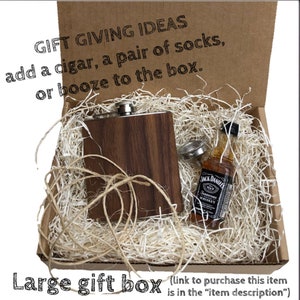 May include: A brown wooden box with a brown and silver flask and a small bottle of Jack Daniel's Tennessee Whiskey inside. The box is filled with shredded paper. The text "GIFT GIVING IDEAS add a cigar, a pair of socks, or booze to the box." is printed on the top of the box. The text "Large gift box (link to purchase this item is in the "item description")" is printed below the box.
