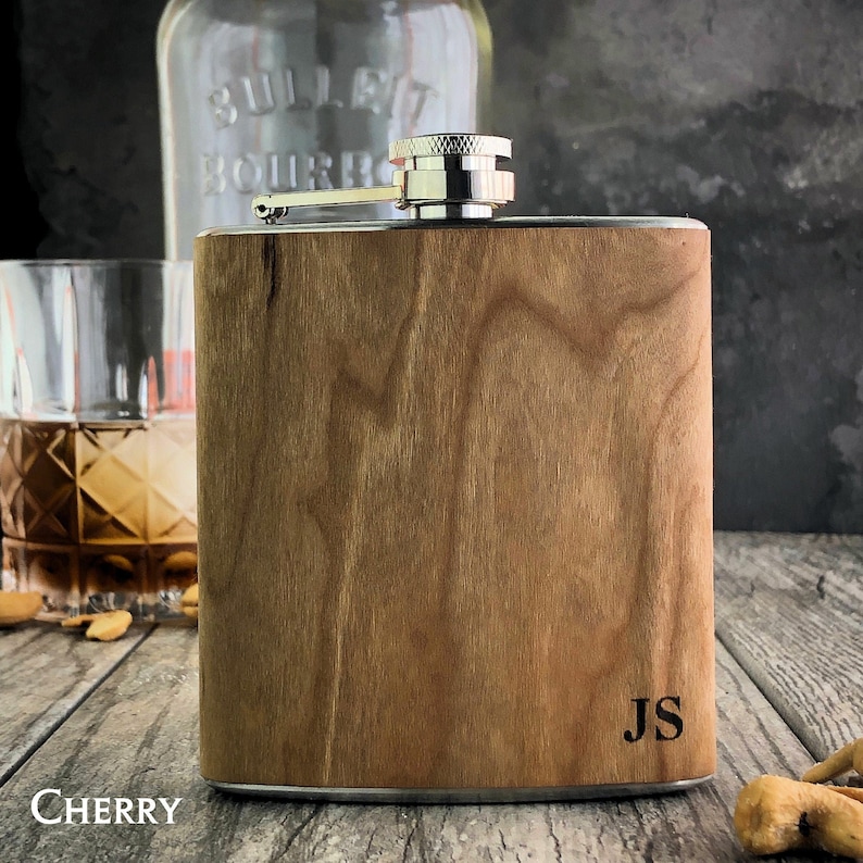 May include: A personalized wooden flask with a silver top and the initials "JS" engraved on the front. The flask is made of cherry wood and has a natural wood grain.