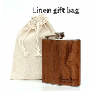 Pu&ograve; includere: Una fiaschetta di legno marrone con un tappo in acciaio inossidabile e un sacchetto regalo in lino. La fiaschetta ha il testo "wickensnuffers" e "www.wickensnuffers.com" inciso sul fondo.