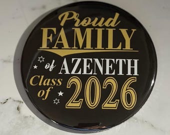 May include: A round, black button with gold and white text. The text reads "Proud FAMILY of AZENETH Class of 2026" with star accents. The button is likely a graduation keepsake or celebratory item.