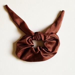 May include: A brown fabric hair scrunchie with a knotted bow detail.