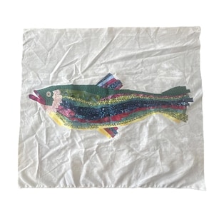 May include: A colorful fish applique on a white background. The fish is made of layered fabric strips in shades of green, blue, yellow, and red. The fish has a pink mouth and a yellow belly. The background is a white, textured fabric.