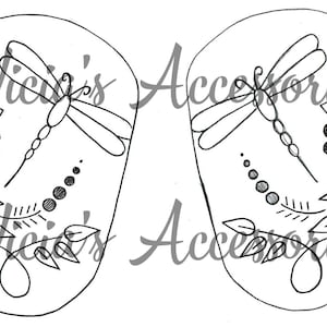 May include: Two matching, black and white, oval-shaped designs featuring a dragonfly, a sunflower, and leaf details. The text "Vicki's Accessories" is written in cursive across the designs.