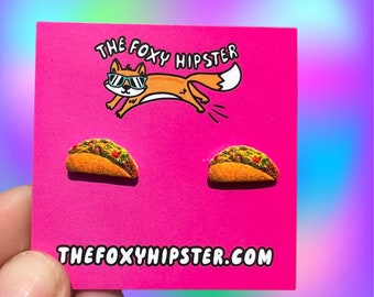 May include: A pair of taco earrings on a pink card with the text "THE FOXY HIPSTER" and "THEFOXYHIPSTER.COM".
